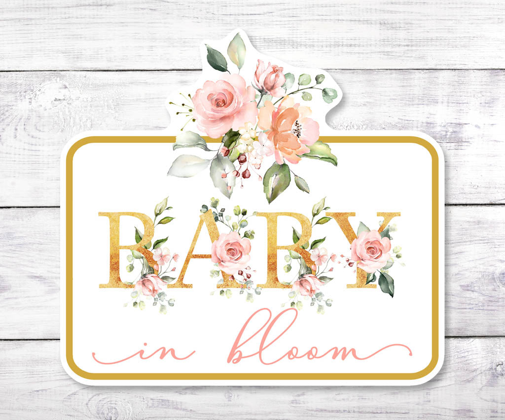 Printable Baby in Bloom floral cake topper on white wood background, showcasing pink watercolor flowers and faux gold lettering.