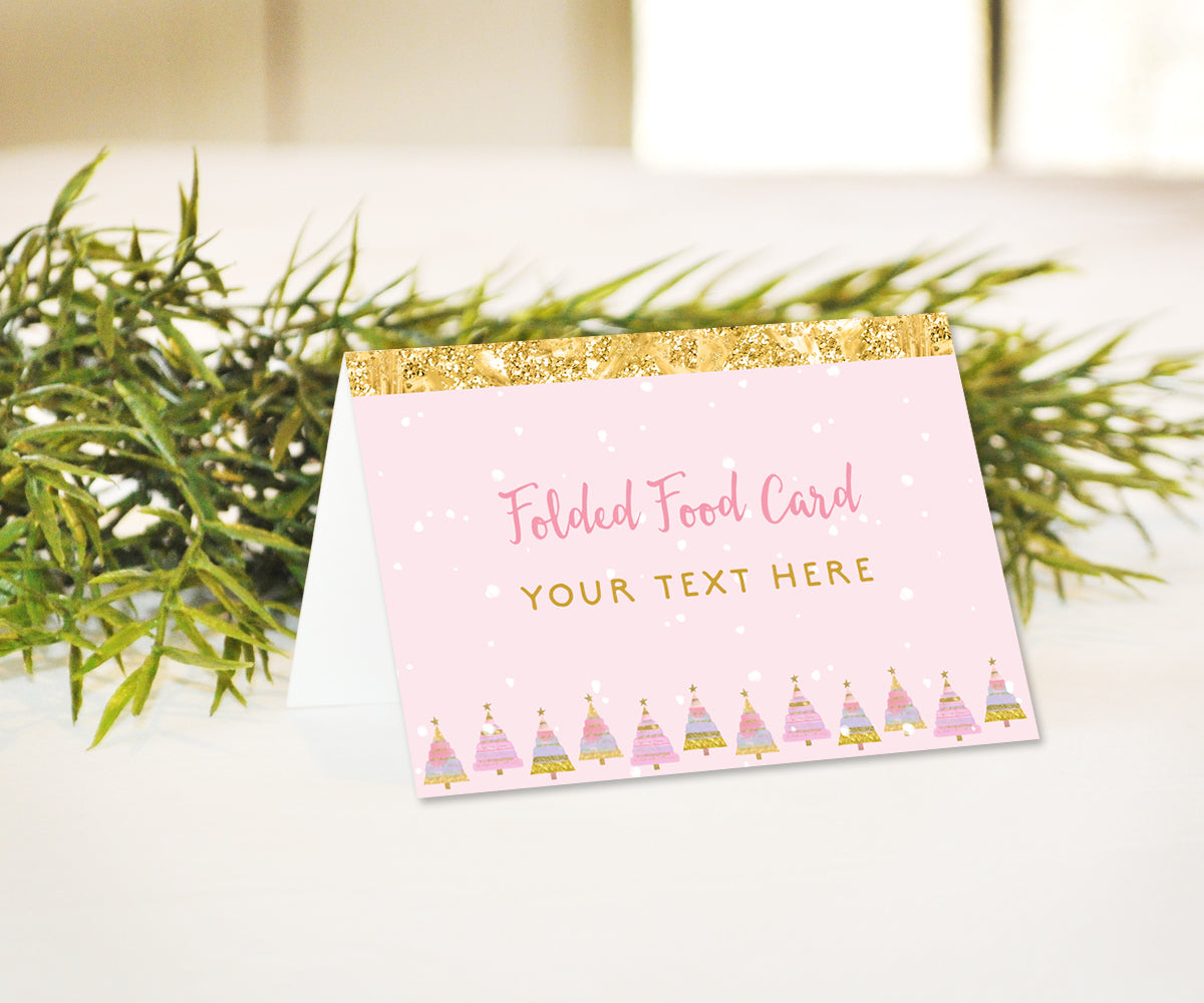 Pink and gold winter birthday party food tent card with snowflakes and festive trees.