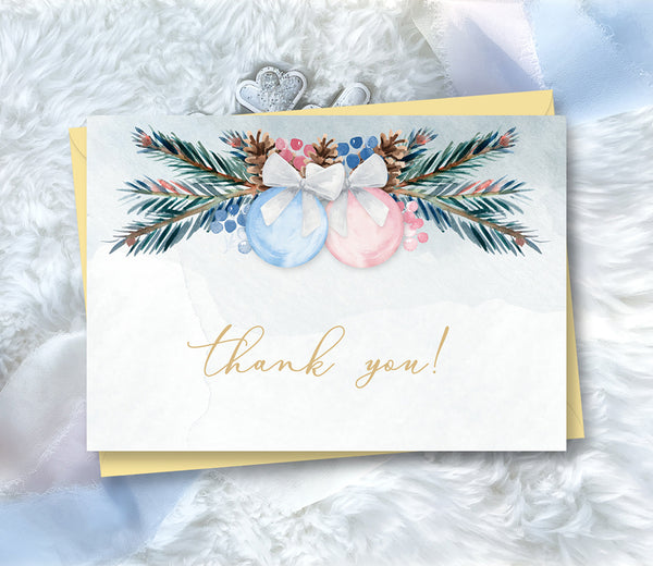Winter Christmas gender reveal thank you card with blue and pink ornaments and greenery.